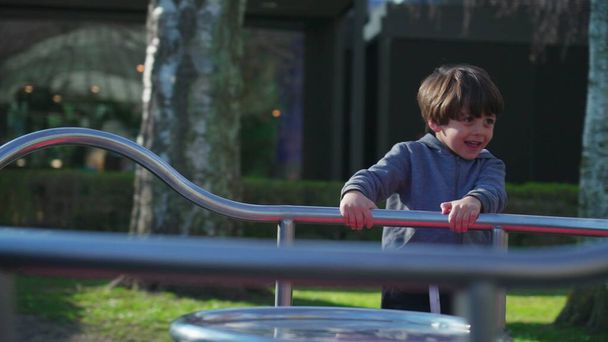 Dziecko bawiące się na placu zabaw karuzeli w sezonie jesiennym. Mały chłopiec kręci się w kółko, trzymając na metalowym pasku ćwiczenia i aktywność na świeżym powietrzu - Zdjęcie, obraz