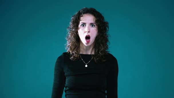 Mujer asombrada con la boca agape en sorpresa, captura de la incredulidad en la cámara contra el fondo Teal - Metraje, vídeo