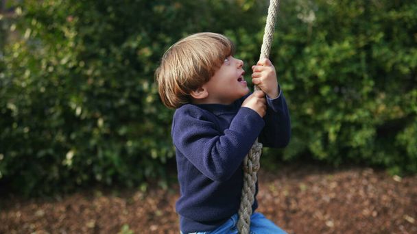 Petit garçon glissant joyeusement le long de la corde métallique entre les arbres dans le parc d'automne - Photo, image