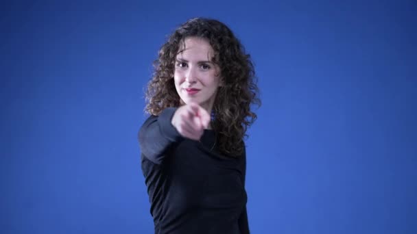 Nainen osoittaa sormella kameraa signaloimalla "Sinä" käsi ele seisoo sinisellä taustalla - Materiaali, video