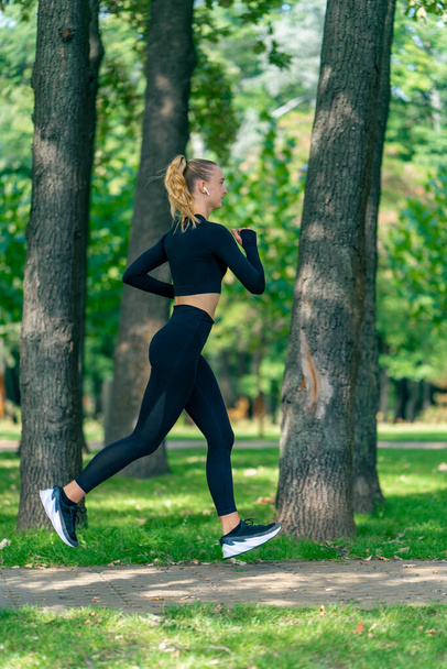 По утрам в парке бегает молодая девушка в спортивной одежде и наушниках для поддержания физической формы. - Фото, изображение
