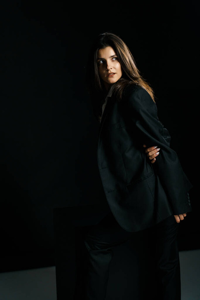 Chica elegante posando en un traje negro y camisa blanca en un estudio de fotografía profesional. Concepto de tiro de moda - Foto, imagen