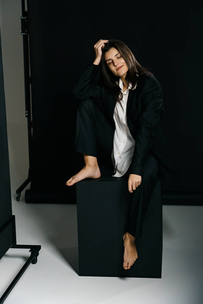 Стильная девушка позирует в черном костюме и белой рубашке в профессиональной фотостудии. Концепция модной съемки - Фото, изображение