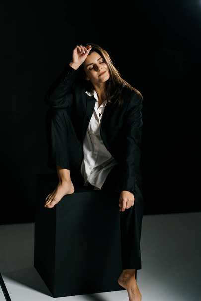 Κομψό κορίτσι ποζάρει με μαύρο κοστούμι και λευκό πουκάμισο σε επαγγελματικό φωτογραφικό στούντιο. Έννοια λήψης μόδας - Φωτογραφία, εικόνα