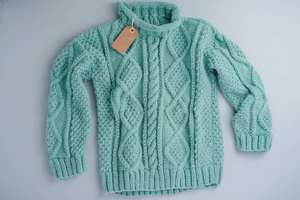 Бирюзовый свитер вязанный шерстяной с биркой на сером фоне, изолированный. Высокое качество фото - Фото, изображение