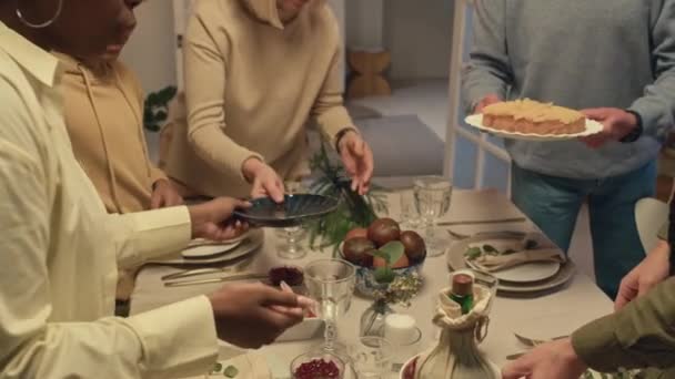 Colpo ritagliato di persone multietniche che sostituiscono insalata, torta e piatti sul tavolo mentre si preparano per la cena festiva a casa. - Filmati, video