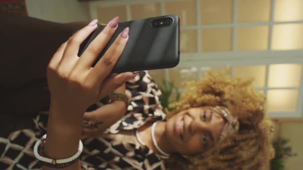 Вертикальний знімок молодої афроамериканської дівчини, яка спілкується зі своїм другом під час відеодзвінка, використовуючи смартфон вдома - Кадри, відео