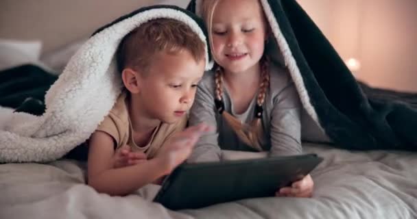 Sonrisa, tableta y niños en la cama con manta relajante, vinculación y haciendo elearning en línea. Feliz, la tecnología digital y los niños que ponen y juegan juegos en el dormitorio juntos en fin de semana en casa por la noche - Imágenes, Vídeo