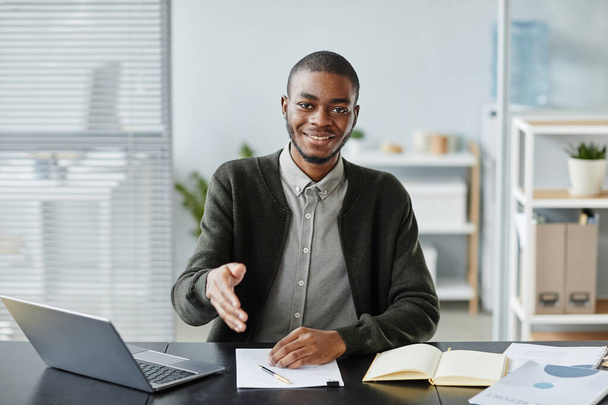 Vorderseite Porträt eines jungen schwarzen Mannes, der im Bewerbungsgespräch in die Kamera lächelt und zur Begrüßung die Hand hält - Foto, Bild