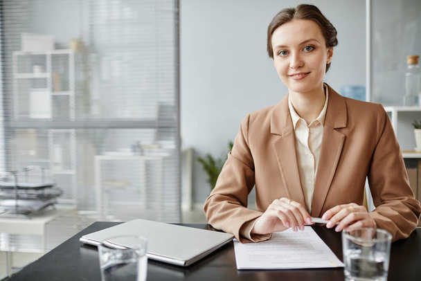 Portrait minimal d'une jeune femme d'affaires souriante portant un costume assis sur le lieu de travail au bureau, espace de copie - Photo, image