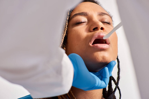 若いアフリカ系アメリカ人女性患者 ヘルスケアの喉を調べる医師の視点が - 写真・画像