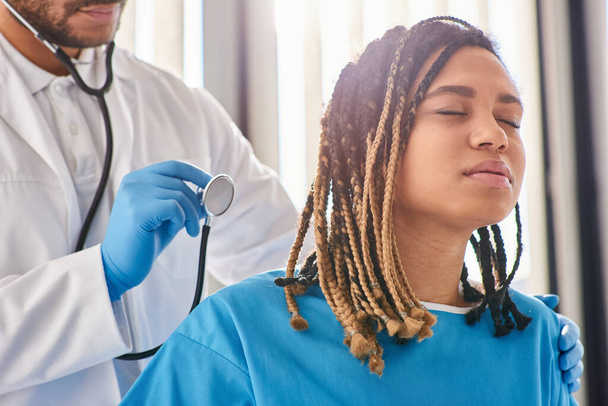 médico indiano ouvir respiração de seu paciente afro-americano doente com estetoscópio, cuidados de saúde - Foto, Imagem