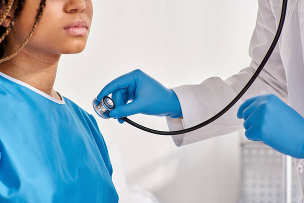 médico indio escuchando el aliento de su paciente afroamericano enfermo con estetoscopio, recortado - Foto, Imagen