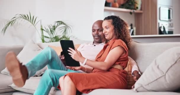 Smile, tablet and funny couple on sofa in home, communication and watch comedy movie, video or meme. Interracial man, woman and laugh on technology, relax on couch and social media app in living room. - Footage, Video