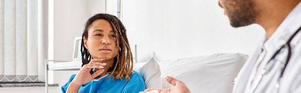 mujer afroamericana en cama de hospital mirando a su médico indio tomando notas en la tableta, pancarta - Foto, imagen