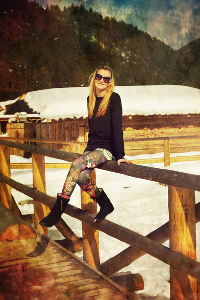 Una bella giovane signora bionda posa su una balaustra di legno in un paesaggio invernale innevato
 - Foto, immagini