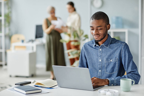 Retrato de un joven negro usando un ordenador portátil en el lugar de trabajo de la oficina en el interior mínimo, espacio de copia - Foto, imagen