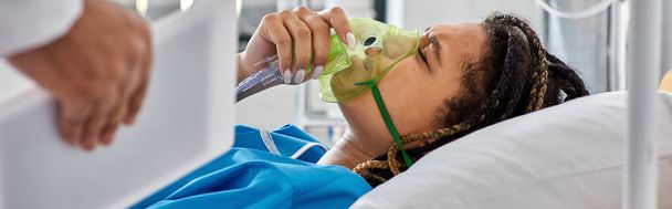 καλλιεργημένη άποψη του γιατρού παρήγορο άρρωστος αφροαμερικανός γυναίκα που βρίσκεται στο κρεβάτι με μάσκα οξυγόνου, πανό - Φωτογραφία, εικόνα