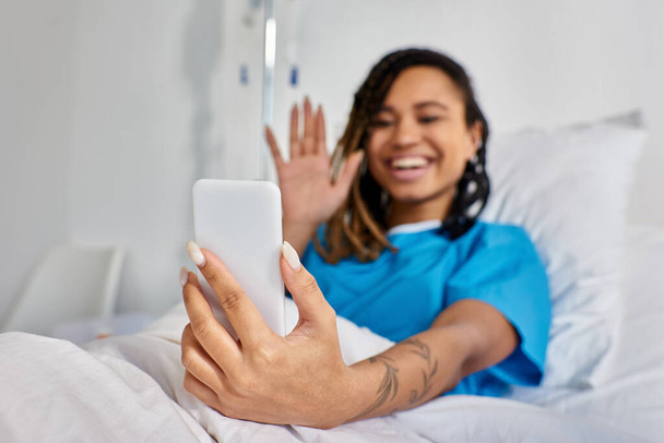 attractive young african american woman having video call while lying in hospital bed, healthcare - Photo, Image