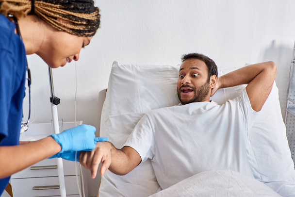 jovem enfermeira afro-americana inserir cateter no braço de seu doente paciente indiano, cuidados de saúde - Foto, Imagem