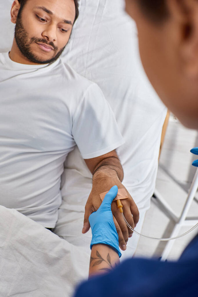 bijgesneden beeld van Afro-Amerikaanse verpleegster invoegen katheter in arm van haar Indiase patiënt, gezondheidszorg - Foto, afbeelding