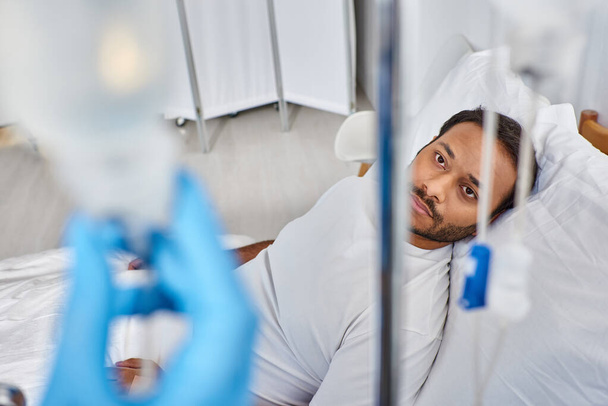 se centran en el hombre indio enfermo acostado en la cama del hospital en la sala y mirando a la cámara a través de mostradores de gota - Foto, Imagen