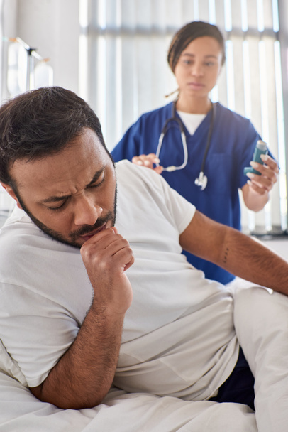 νεαρή Αφροαμερικανή νοσοκόμα που δίνει εισπνοές άσθματος στον άρρωστο Ινδό ασθενή της στο θάλαμο του, την υγειονομική περίθαλψη. - Φωτογραφία, εικόνα