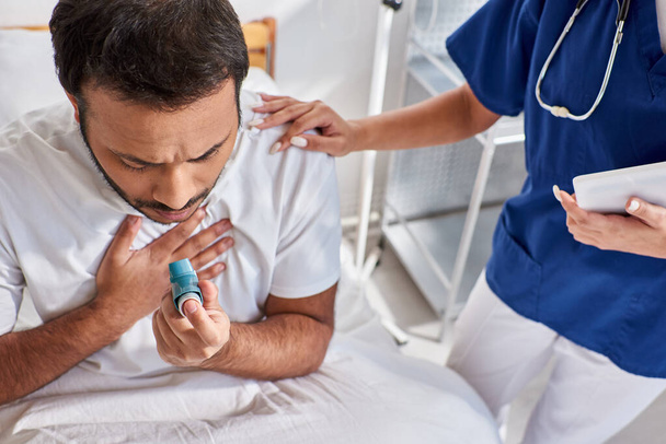 Afrykańska pielęgniarka amerykańska pomaga indyjskiemu pacjentowi z inhalatorem astmy na oddziale szpitalnym - Zdjęcie, obraz