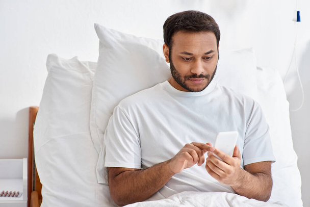 paciente indio concentrado acostado en la cama de hospital en su sala con teléfono en las manos, atención médica - Foto, imagen