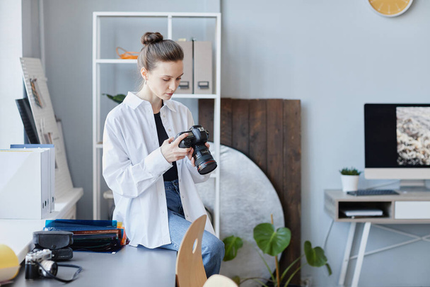 Retrato de una joven fotógrafa mirando imágenes de la cámara en un entorno de estudio mínimo, espacio de copia - Foto, Imagen