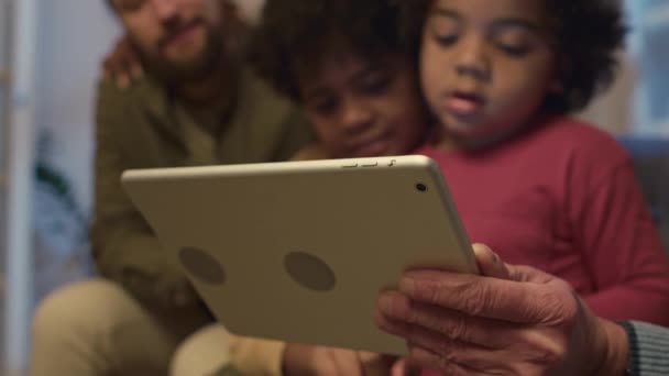 Focus op digitale tablet, kinderen en ouders die tablet vasthouden terwijl ze tijd samen doorbrengen binnen - Video