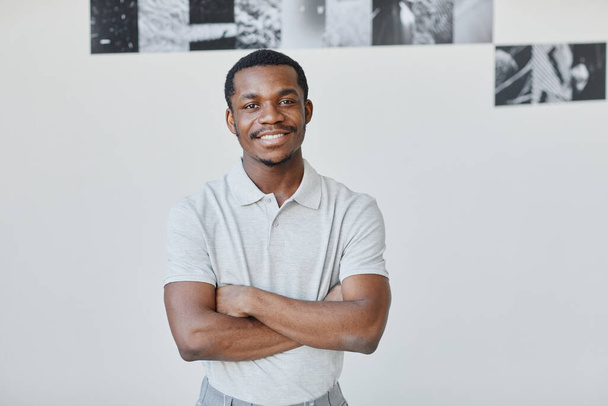 Minimalny portret w pasie w górę młodego czarnego artysty uśmiechniętego do aparatu, stojącego z rękami skrzyżowanymi w sali galerii, przestrzeń do kopiowania - Zdjęcie, obraz