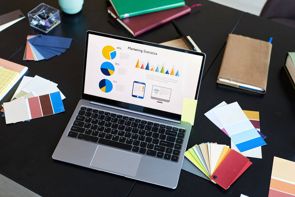 Boven hoek van laptop met financiële informatie op het scherm staan op de werkplek van ontwerper of econoom onder pakettes en notebooks - Foto, afbeelding