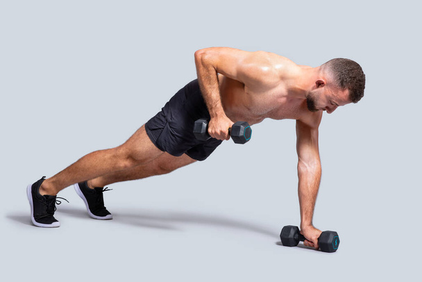 Hombre europeo milenario muscular fuerte hacer ejercicios con pesas, flexiones para bíceps, aislado en fondo gris estudio. Entrenamiento atlético de fuerza, cuidado corporal y potencia - Foto, imagen