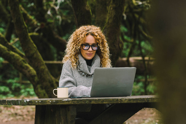 Digital nomad traveler people concept work lifestyle. Alternative outside office in the nature. Pretty woman in smart working on laptop sitting in the woods. Female people enjoying online connection - Foto, Bild