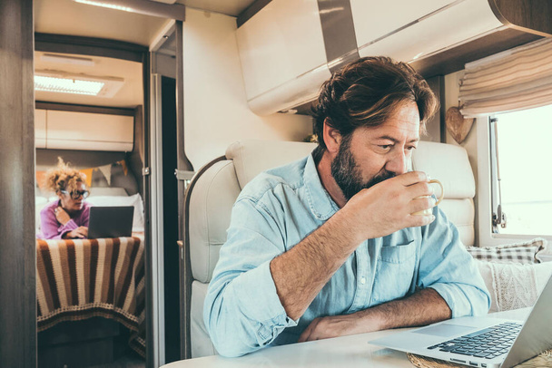 Couple use computer inside camper van during travel vacation or van life lifestyle. Modern man and woman work together on laptop in alternative office motor home. Digital nomad and smart free working - Photo, image