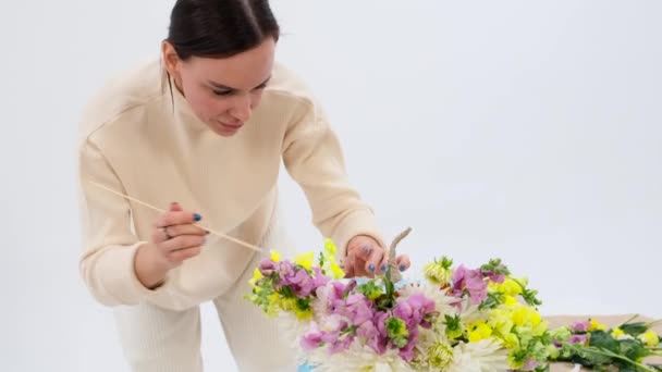Skilled Caucasian florist passionately works on crafting beautiful bouquets inside hollowed out pumpkins against a pristine white backdrop. Her hands move with grace and expertise. - Footage, Video