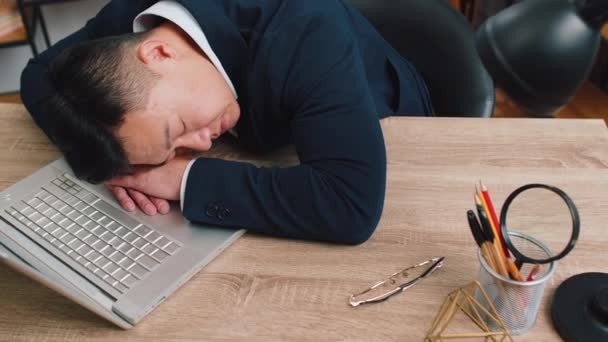 Sıkıcı Asyalı iş adamı dizüstü bilgisayarda çalışıyor, ofis masasında el ele uyuya kalıyor. Yorgun, serbest çalışan, orta yaşlı, işkolik bir adam. İstihdam, meslek, işsiz - Video, Çekim
