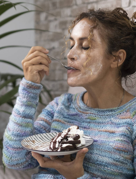  жінка вдома насолоджується смачним тортом з вершками та шоколадом із задоволенням висловлюється на обличчі. Жінки розслабляються вдома. Концепція їжі та щастя. Молода доросла леді на дивані - Фото, зображення