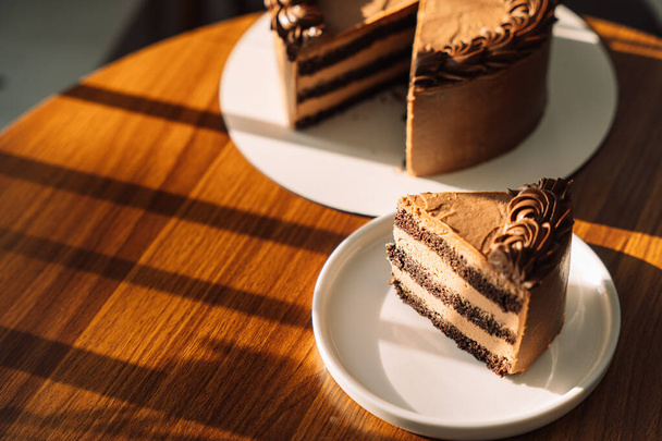 Kawałek czekolady z ciasta na białym talerzu na drewnianym stole. - Zdjęcie, obraz