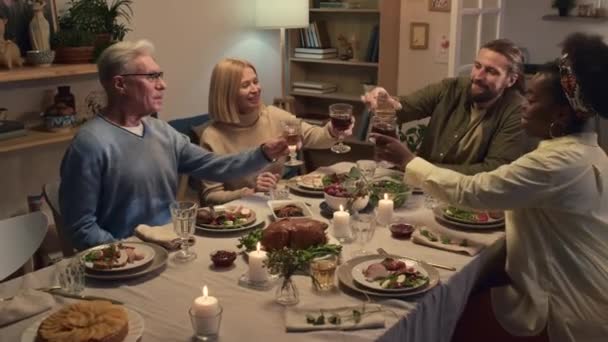 Membri della famiglia interculturale di moglie, marito e genitori che si accoppiano bicchieri di vino mentre festeggiano il Giorno del Ringraziamento a casa - Filmati, video