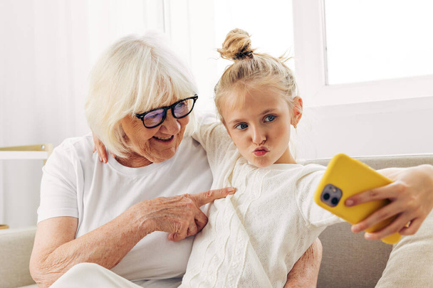 Селфи улыбающийся ребенок вместе диван видео телефон два копия обучения связи обнимая внучку семья футболки люди белые фотографии называют пространство в помещении бабушка - Фото, изображение