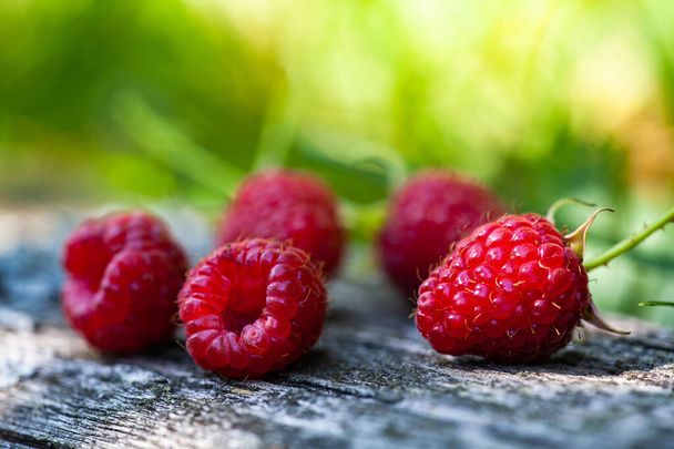 Juicy, just harvested raspberries arranged on a weathered, vintage wooden tabletop. Ripe red raspberry berries, lie on a wooden background. Selective focus - Photo, Image