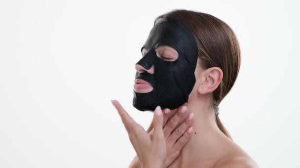Кавказька жінка носить чорну маску для обличчя, очі відображають відчуття спокою і самодопомоги на чистому білому тлі. Маска покращує свої особливості, підкреслюючи відданість скінарію. - Кадри, відео