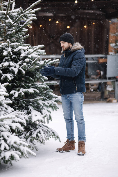 Handsome man measuring Christmas tree outdoor. Man choose fir tree for winter holidays. - Photo, Image