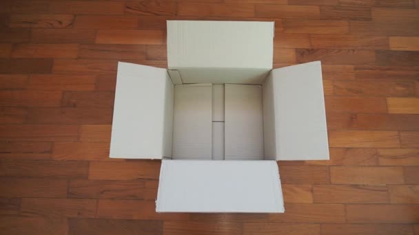 caja de cartón abierta sobre piso de madera - Metraje, vídeo