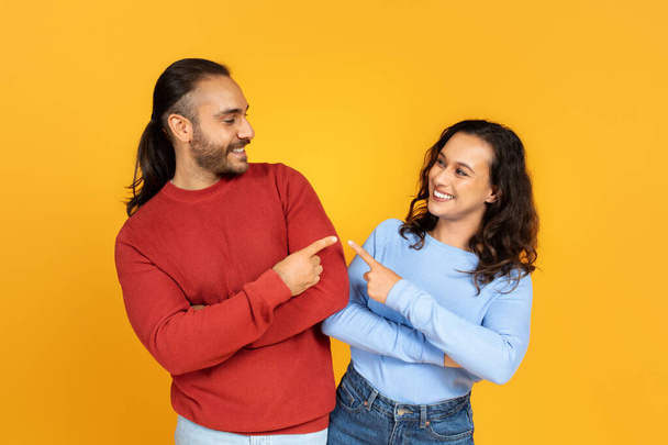 Positives Millennial-Paar, das auf einander zeigt und lächelt, fröhlicher junger Mann und Frau, die sich isoliert auf gelbem Studiohintergrund amüsieren. Liebe, Beziehungen, Freundschaft - Foto, Bild