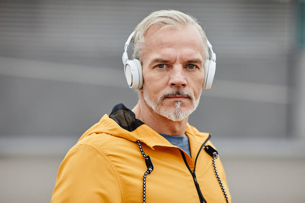 Portrait of handsome mature man wearing headphones outdoors and looking at camera in urban city setting, copy space - Foto, Bild