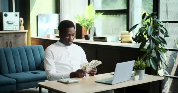 Een Afro-Amerikaanse man gooit speels een stapel geld in de lucht, en zijn vrolijke glimlach wordt vastgelegd als hij in de camera kijkt. Deze scène straalt een gevoel van financieel vertrouwen en positiviteit uit. - Video