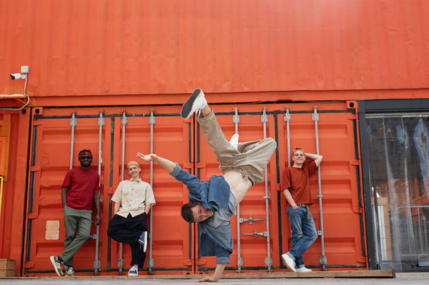 Filmagem de movimento de toda a equipe de dança masculina realizando hip-hop e breakdance no cenário urbano da cidade, foco no homem fazendo pose de suporte - Foto, Imagem